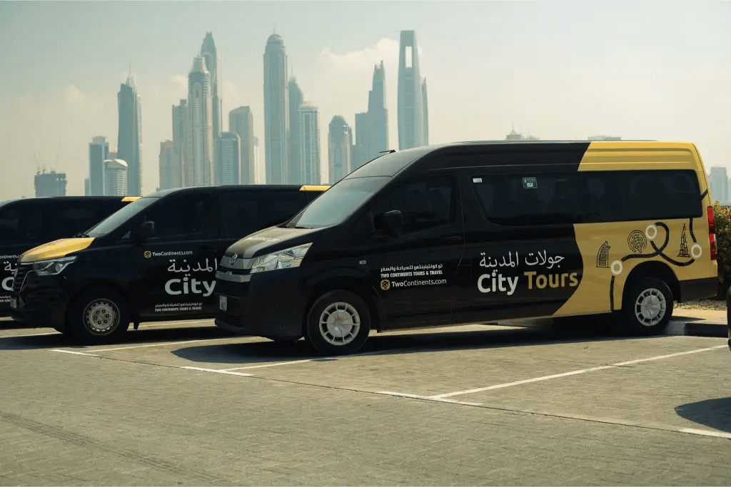 A row of black and yellow 'City Tours' vans, branded with the TwoContinents logo, parked with the modern Dubai city skyline in the background.