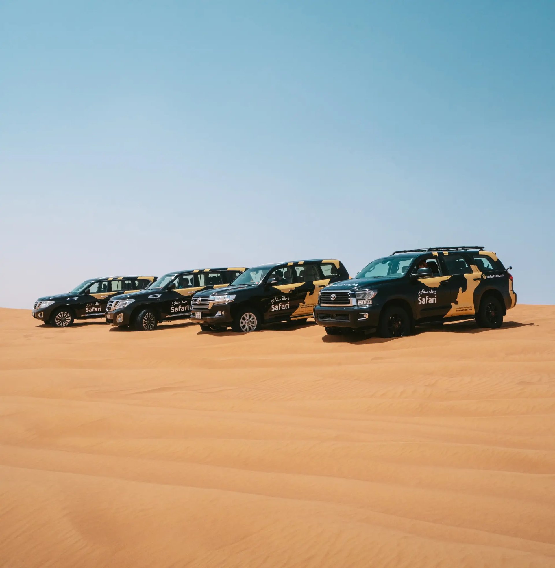A lineup of four branded 'Safari' SUVs parked on a golden sand dune under a clear, bright blue sky.
