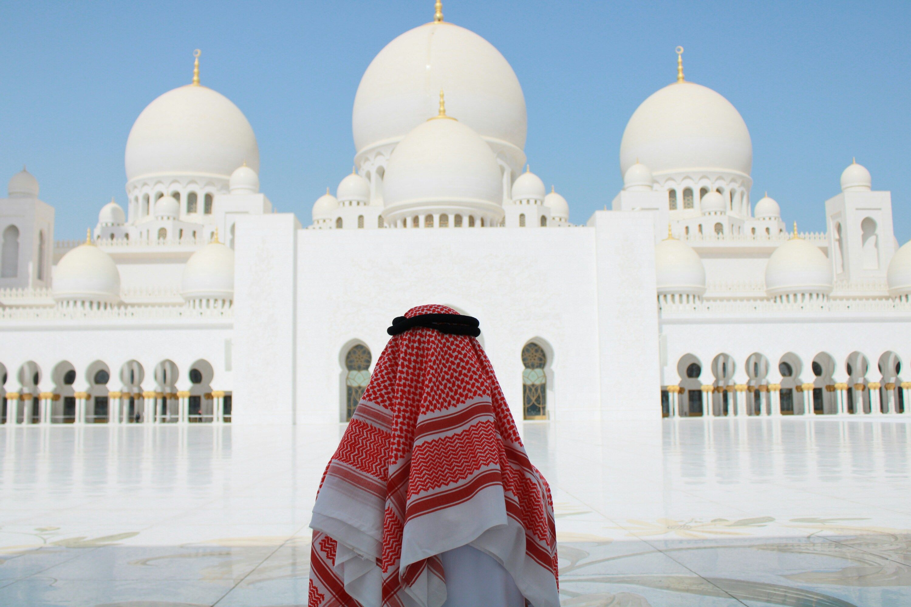 Sheikh Zayed Grand Mosque in Abu Dhabi with white domes and courtyard, a person in traditional attire in the foreground.